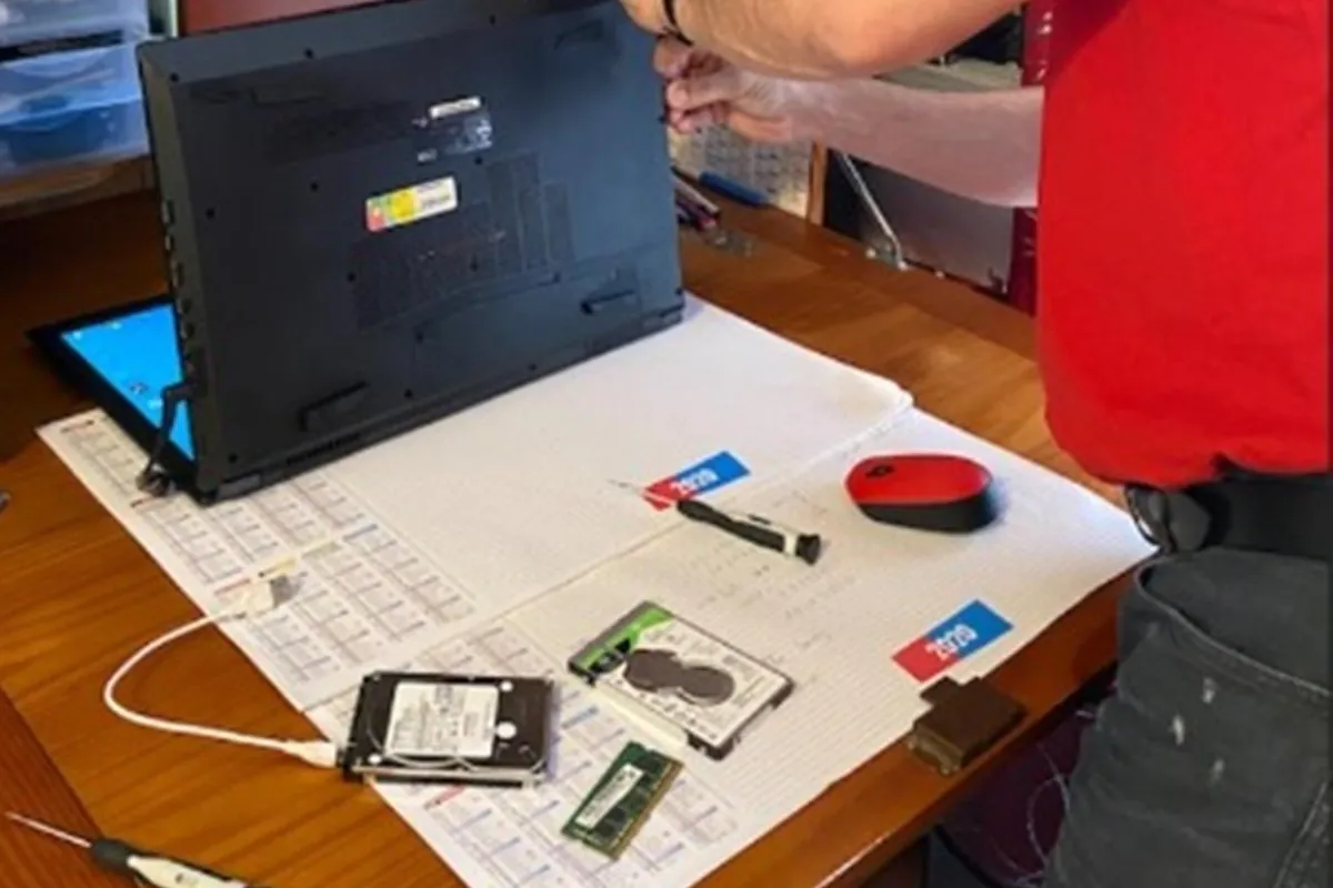 Jean-Paul Marras répare un ordinateur portable : disques durs et barrette de mémoire sur le plan de travail