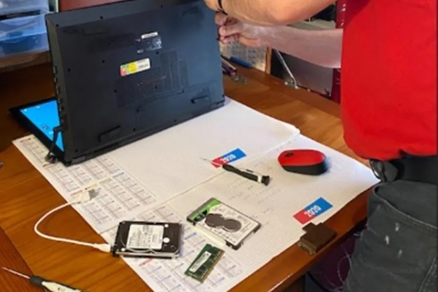 Jean-Paul Marras répare un ordinateur portable : disques durs et barrette de mémoire sur le plan de travail