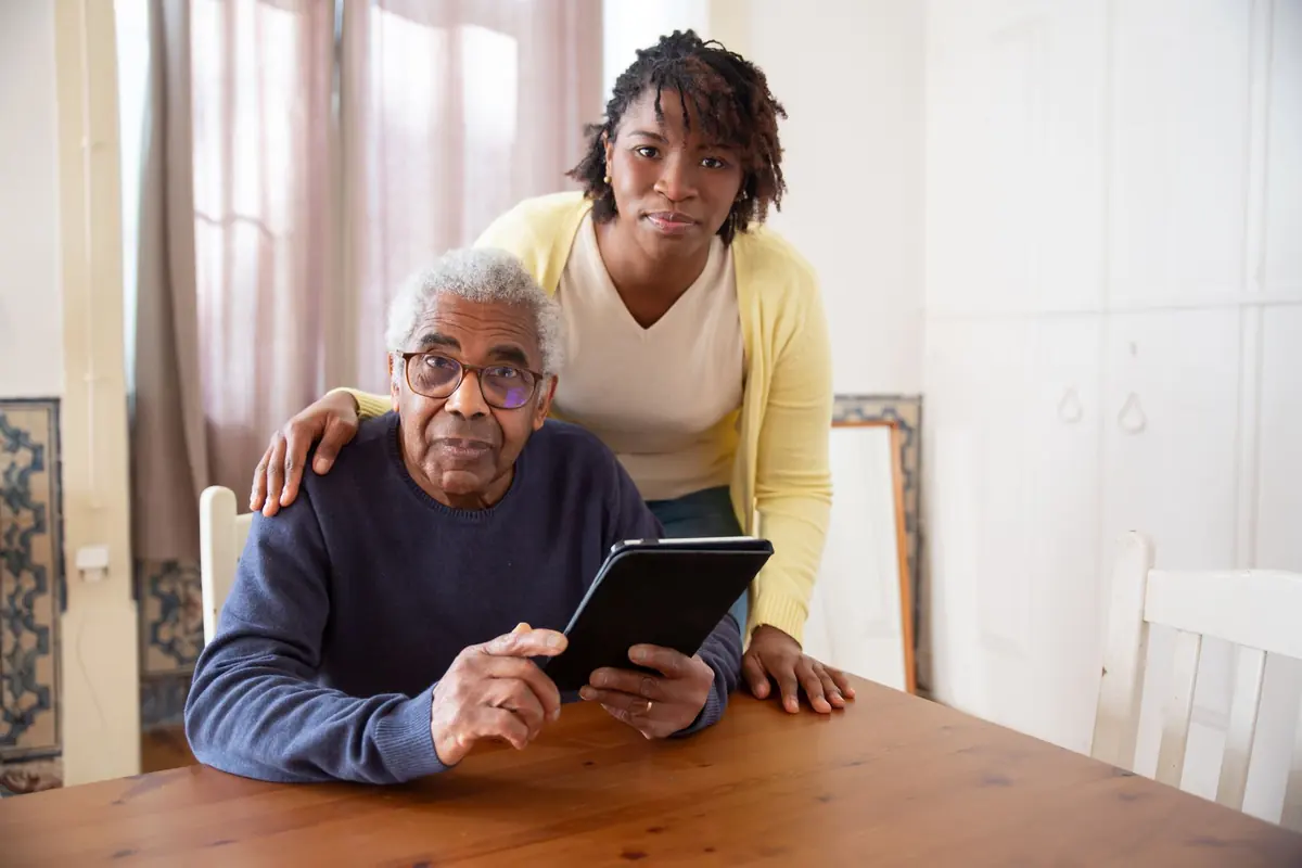 Un technicien aide un monsieur âgé à utiliser sa tablette chez lui